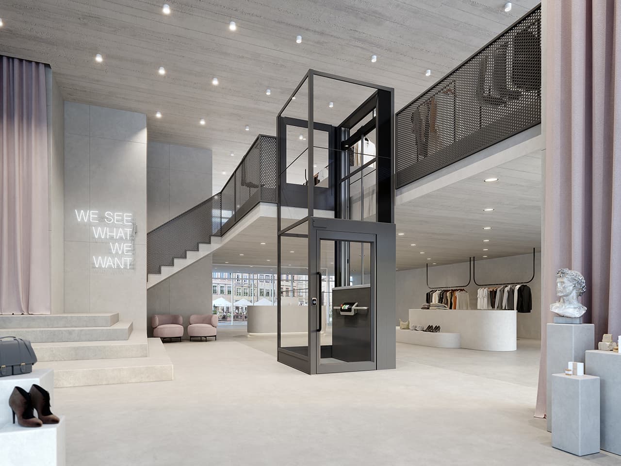 Elegant clothing store with concrete walls, dusty pink accents and furniture and a white neon sign saying "We see what we want", featuring a grey Kalea Luna platform lift with a glass shaft and a gate on the top floor, installed against a loft landing.
