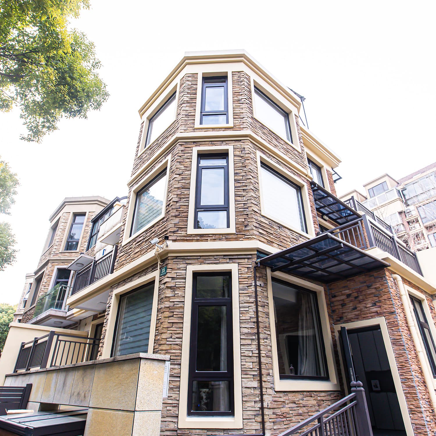 View from below of elegant Shanghai townhouse built in beige bricks against a white sky with green tree branches in the left upper corner of the image.