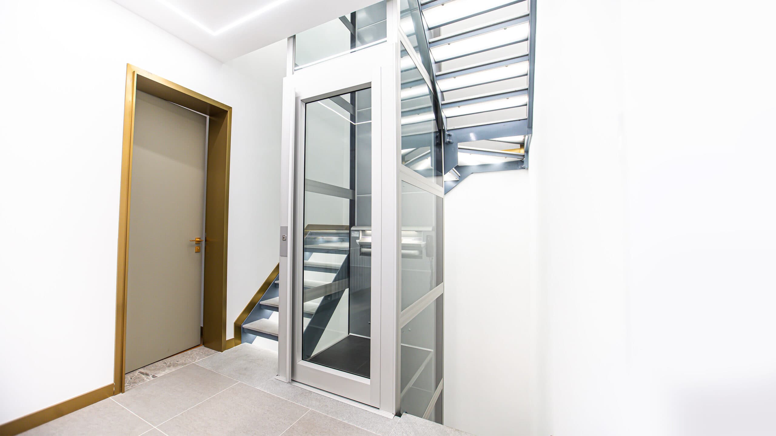 A metallic grey Kalea A4 Mini platform lift installed in a modern townhouse staircase.